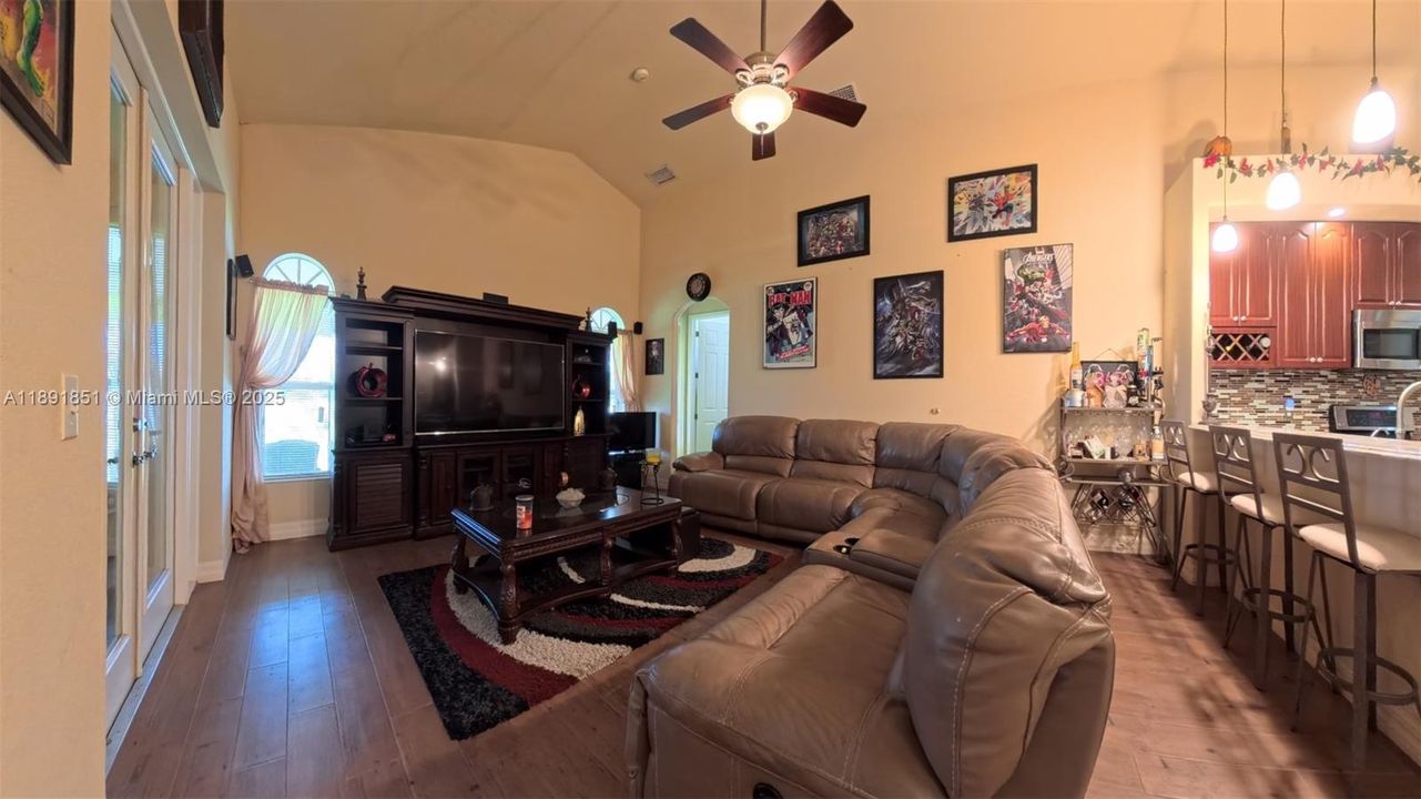Family/entertainment area with wood-tiled floors, ceiling fan, and high vaulted ceiling; off kitchen with breakfast bar.