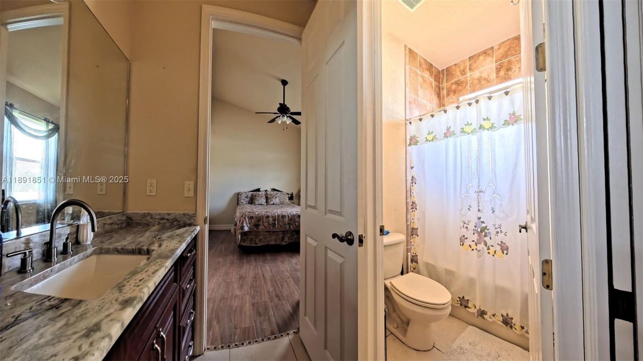Guest bedroom 2 with wood tiled floors, featuring ensuite bathroom with marble vanity, private water closet and shower/bath combination.