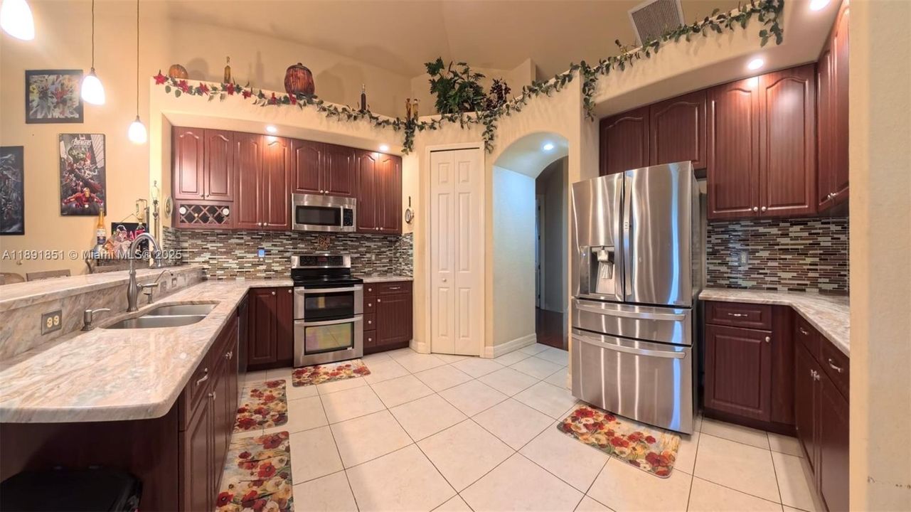Kitchen with stainless steel appliances, granite counters, featuring a peninsula and breakfast bar, decorative backsplash and light fixtures.