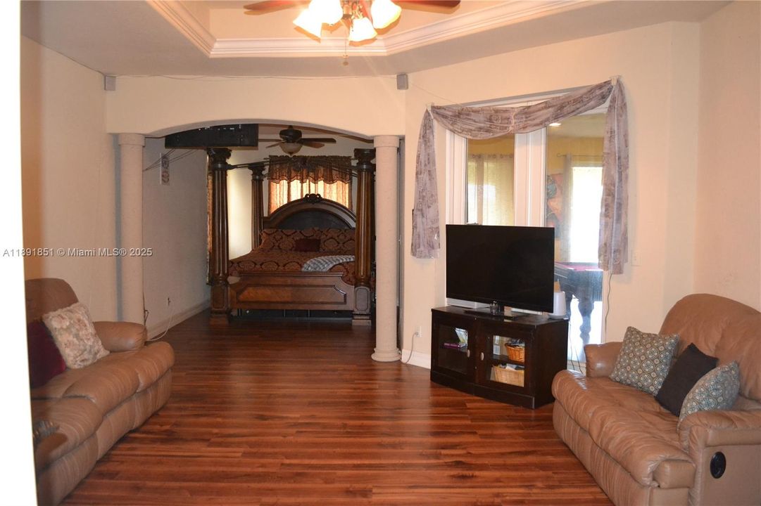 Master bedroom suite with sitting area, featuring wood floors, ornamental molding, a ceiling fan, a raised ceiling, and decorative columns