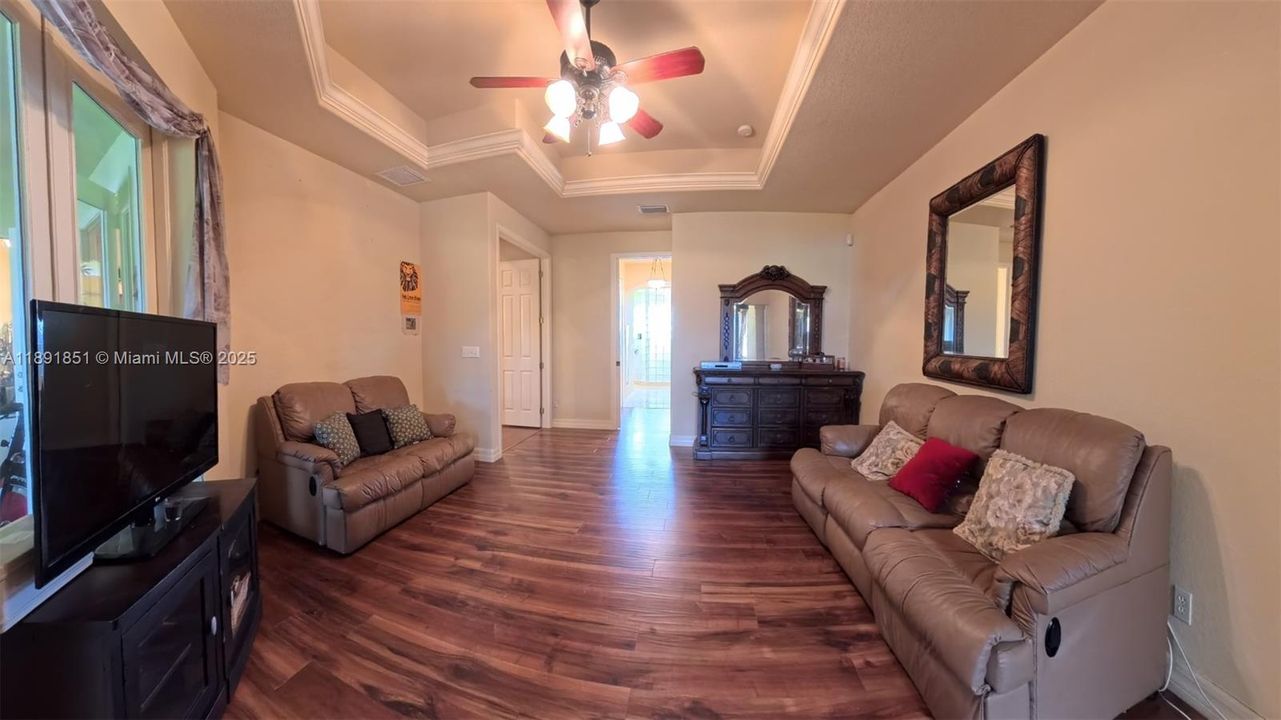 Master bedroom sitting area featuring wood flooring, a raised ceiling, ornamental molding and ceiling fan with passageway to master bath.