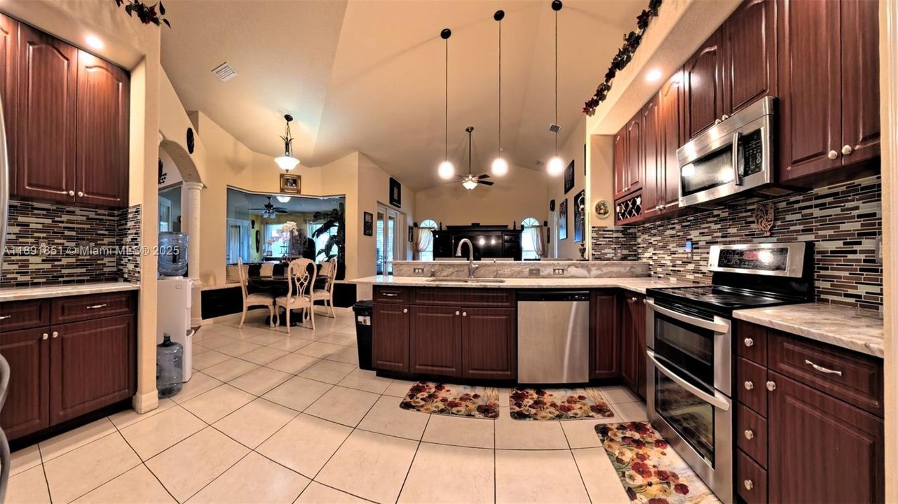Kitchen featuring decorative backsplash, stainless steel appliances, lofted ceiling, dark brown cabinetry, hanging light fixtures, and raised counter breakfast bar plus breakfast area.