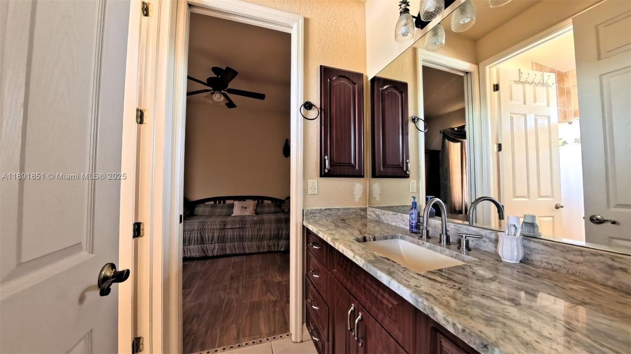 Guest bedroom 1 with ensuite bathroom featuring marble vanity, shower/bath combination with wood tiled floors.
