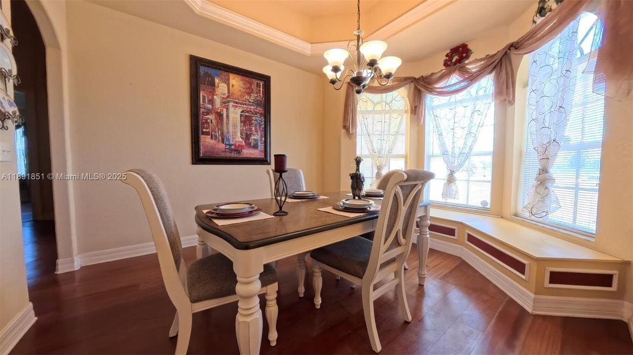 Formal dining room with wood floors, featuring arched walkways, tray ceiling and chandelier plus window storage bench