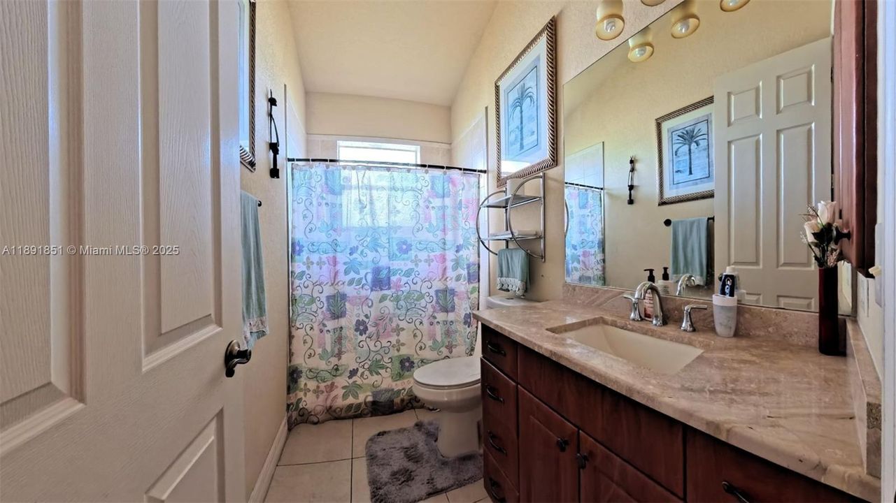 Guest/pool bath featuring vanity with marble top, tiled floors, walk in shower with tiled walls throughout.