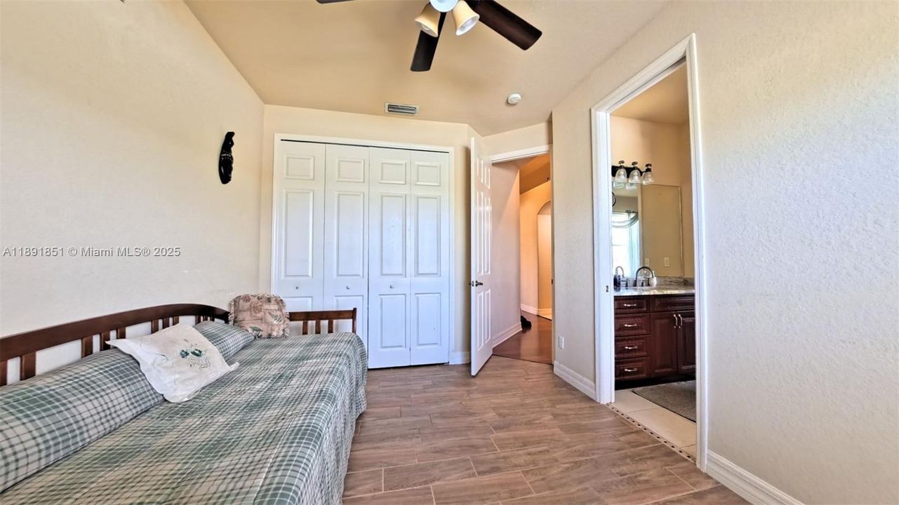 Guest bedroom 1 featuring wood tiled floors, connected bathroom, ceiling fan, and textured wall.