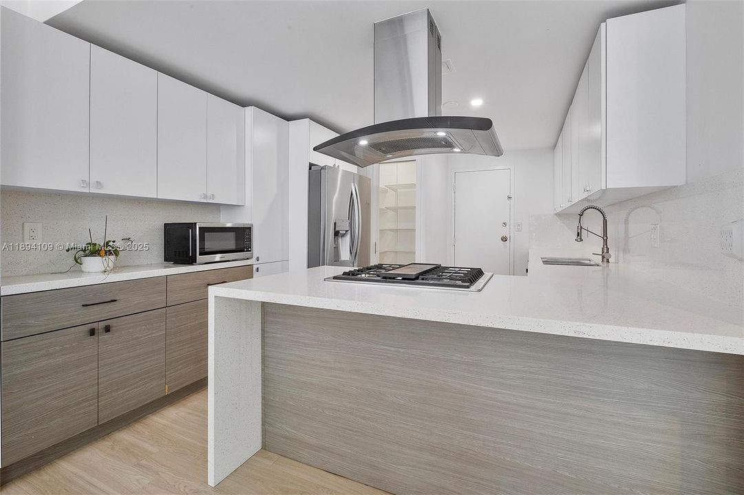 Kitchen details show stainless steel hood, refrigerator and gas range. Recessed lighting beautifies the space.