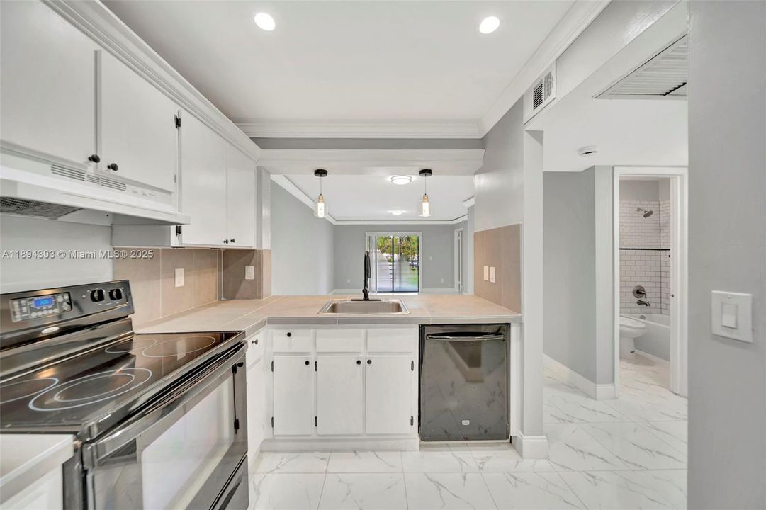 Freshly updated kitchen with stainless steel appliances, modern lighting, and an open view straight into the living room and out to the patio.