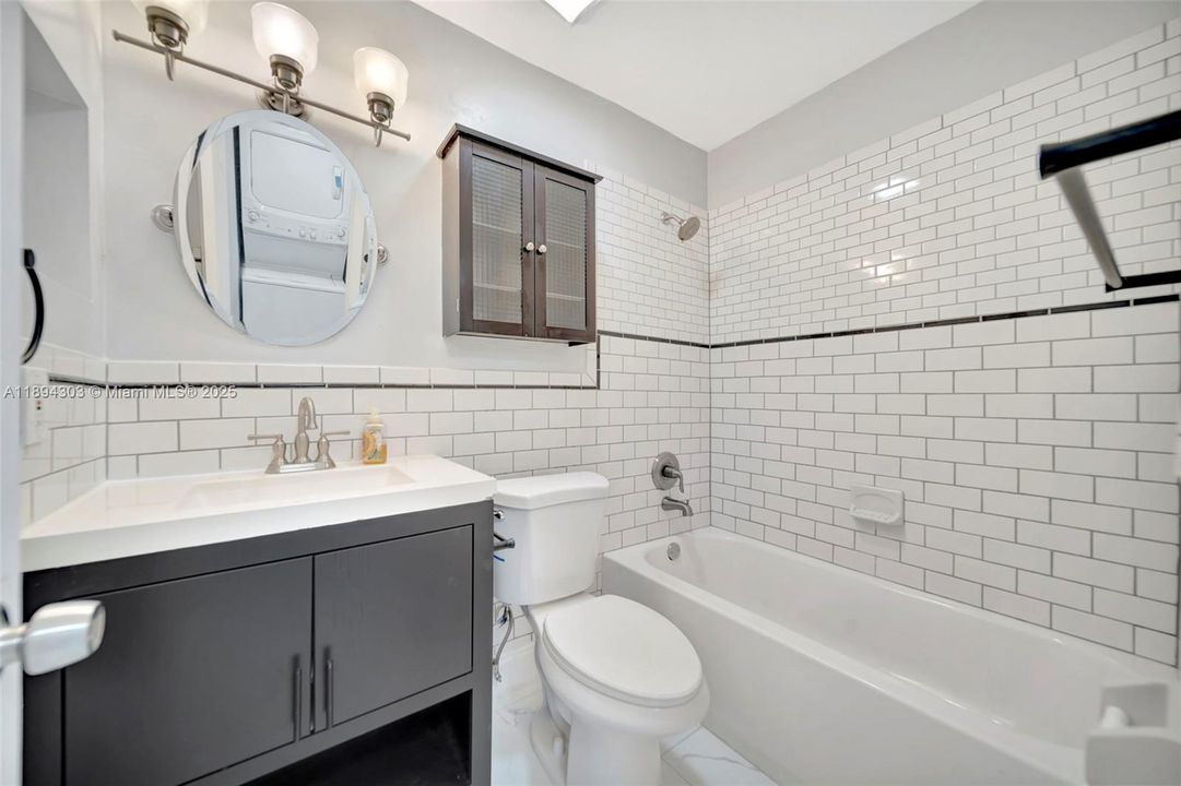Stylish, updated bathroom showcasing classic white subway tile with a contrasting accent band, a modern dark vanity with a crisp white top, designer lighting, and upgraded fixtures. Sophisticated, timeless, and beautifully finished.