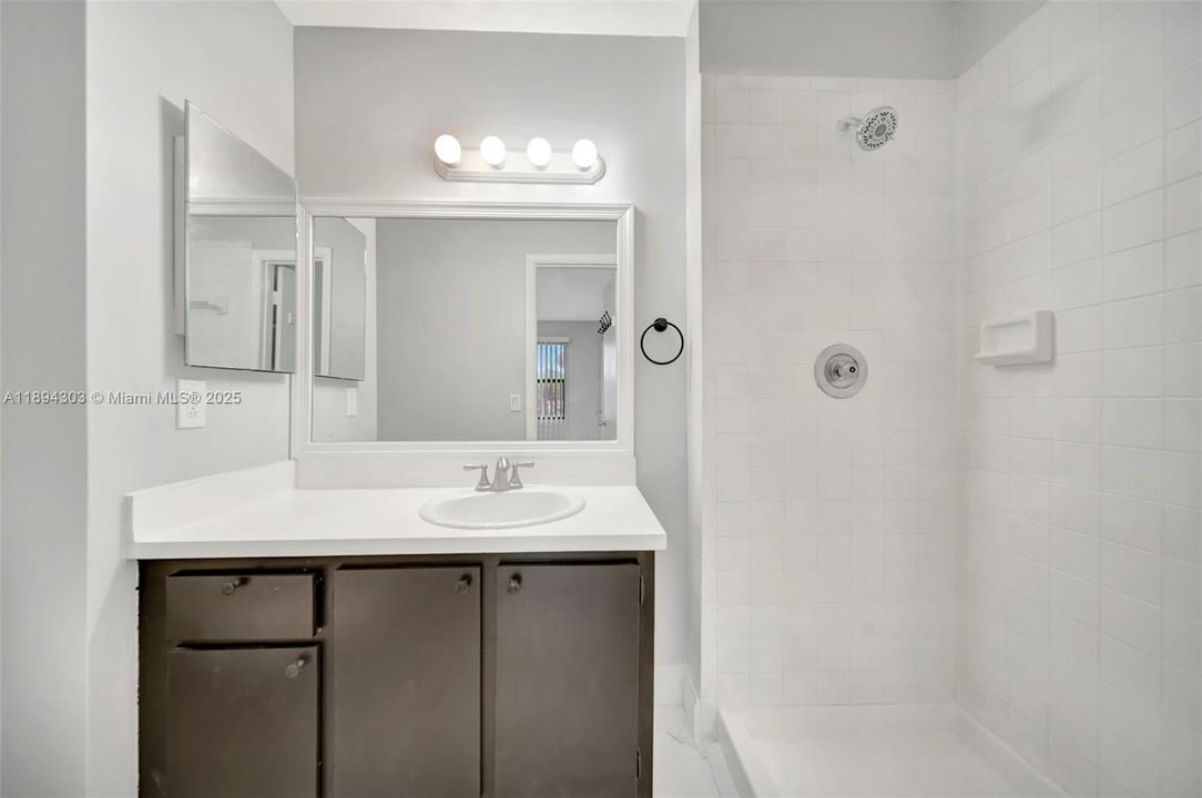 The bathroom is simple, clean, and practical, with a walk-in shower and oversized vanity for storage.