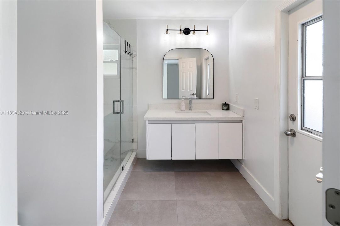 The primary bathroom features clean white finishes and modern fixtures. The door provides easy and convenient access to the pool.
