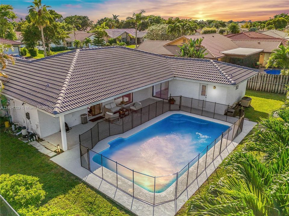 The backyard features a well-maintained rectangular pool, safely enclosed by a fence. A shaded patio area nearby offers a comfortable space for outdoor living, allowing you to relax, dine, or entertain while staying cool and protected from the sun.