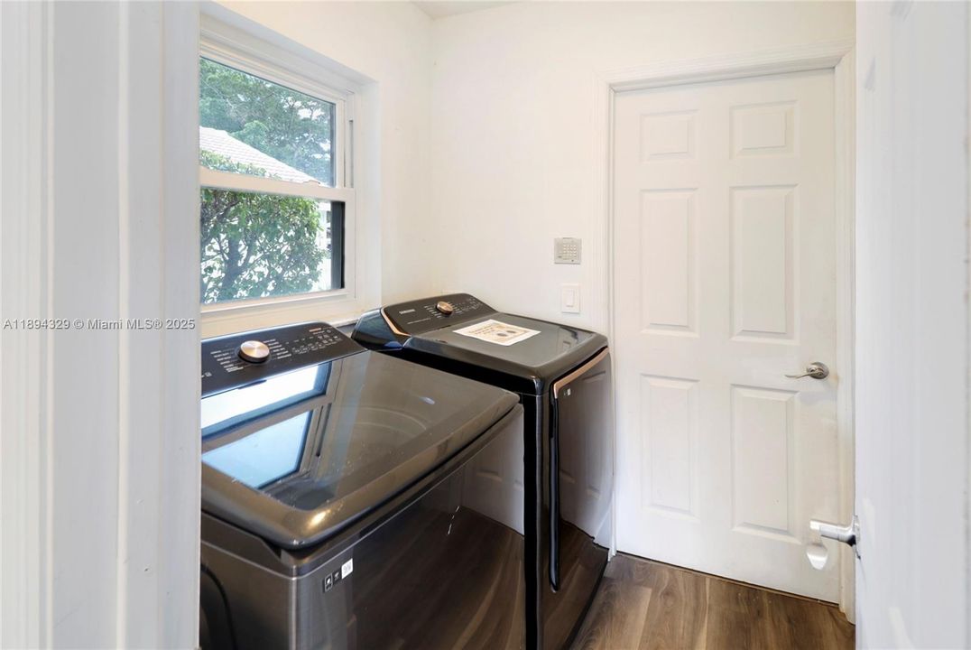This bright and functional laundry space, with a window that allows natural light to filter in, creating an inviting atmosphere. While the washer and dryer are shown for staging purposes, please note they are not included in the sale. Built-in shelving is already in place and thoughtfully serves as a pantry, offering convenient additional storage. Just beyond the appliances, a door leads to the garage, which is currently unavailable for viewing as the family is actively preparing for their move.