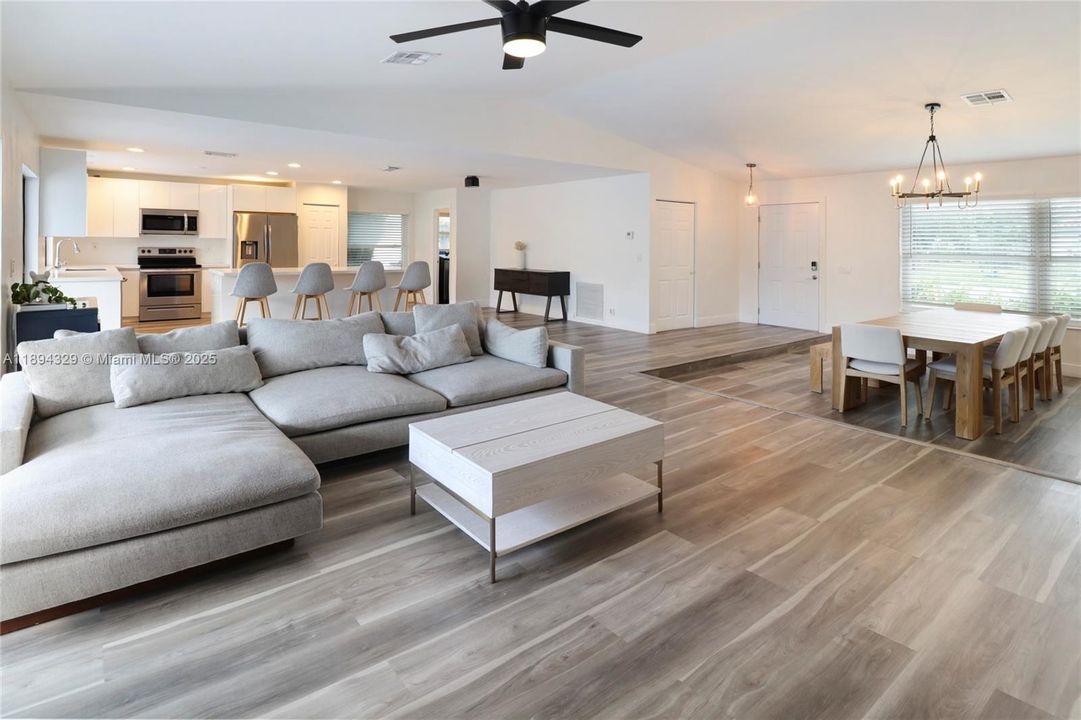 The living room, with its inviting sectional and ottoman, sits beneath expansive windows that flood the area with natural light.