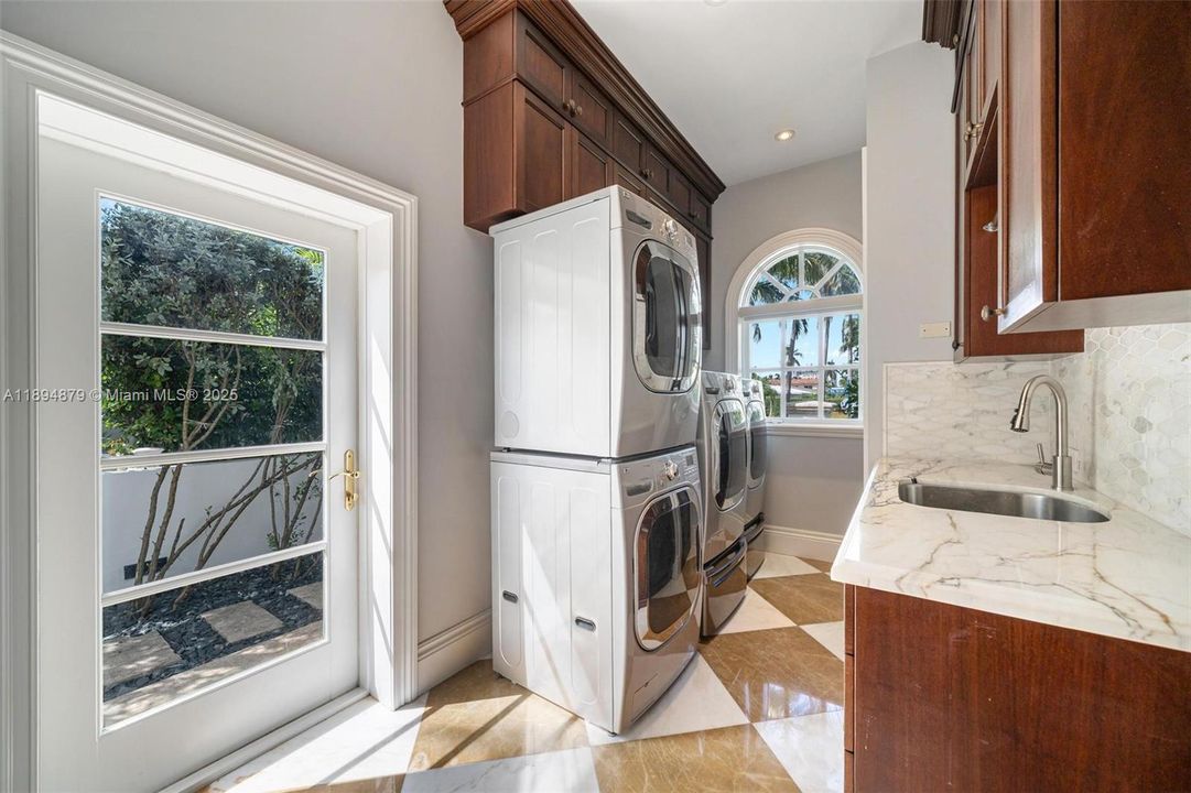 Bright laundry room with dual washer/dryer sets, sink, abundant storage & exterior door