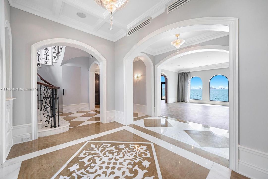 Central foyer with arched openings: stair left, bayfront living/library ahead, corridor to kitchen/dining/media right