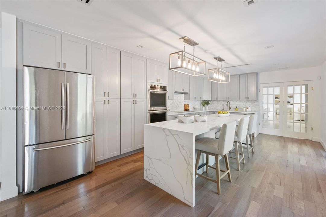 Gourmet kitchen with a large island, custom cabinetry, and stainless steel appliances overlooking the sparkling pool and lush backyard