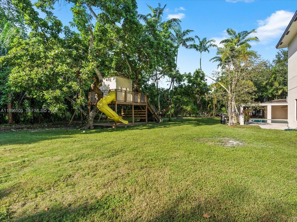 One-acre fenced yard with treehouse, jungle gym, covered outdoor kitchen, and deck — perfect for kids, pets, and entertaining, with space to add a tennis or pickleball court.