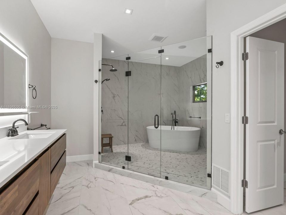 Spa-style primary bath with oversized shower boasting four shower heads, plus a soaking tub with window views — the perfect blend of luxury and relaxation.