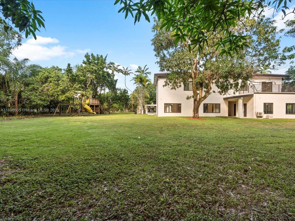 One-acre fenced yard with treehouse, jungle gym, covered outdoor kitchen, and deck — perfect for kids, pets, and entertaining, with space to add a tennis or pickleball court.