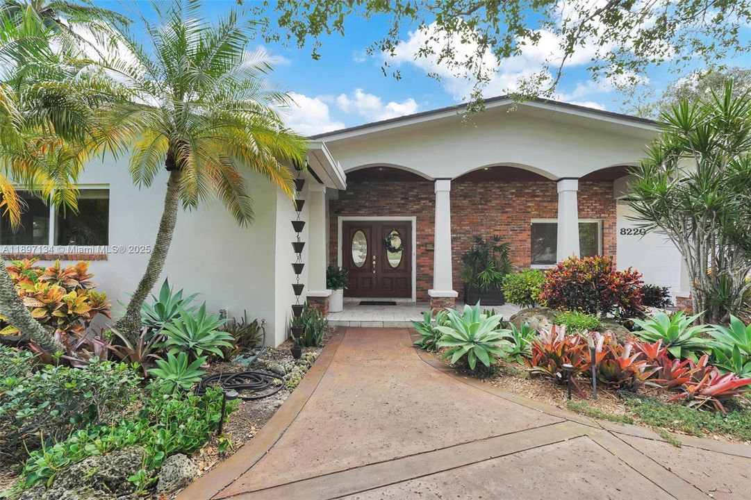 Tropical curb appeal with lush landscaping and elegant double-door entry in Palmetto Bay.
