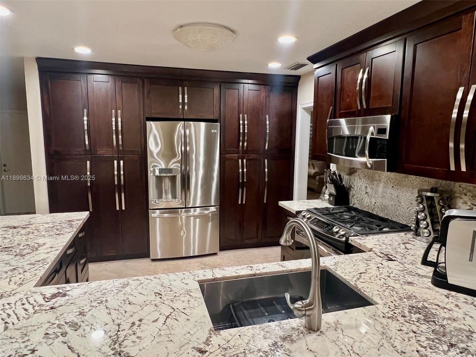 Custom wood cabinets with soft-closing doors and pull out drawers for pantry, stainless steel appliances, gas stove/oven and granite countertops