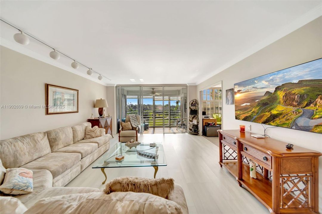 Bright and inviting living room with wide-plank floors, custom lighting, and floor-to-ceiling sliders that frame tranquil golf course and lake views.