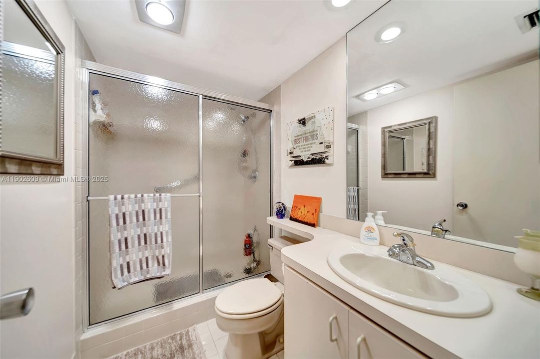 Well-appointed full bath featuring an extended vanity with great counter space, a wide mirror with recessed lighting, and a step-in shower with sliding glass doors for easy access and privacy.