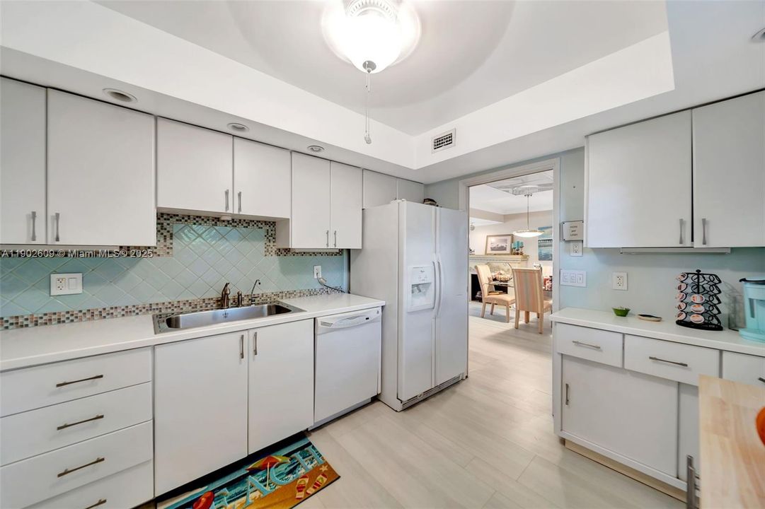 Light, bright, and functional — this kitchen offers extensive cabinet storage, clean white finishes, tile backsplash with accent detailing, and direct access to the dining area for easy entertaining.