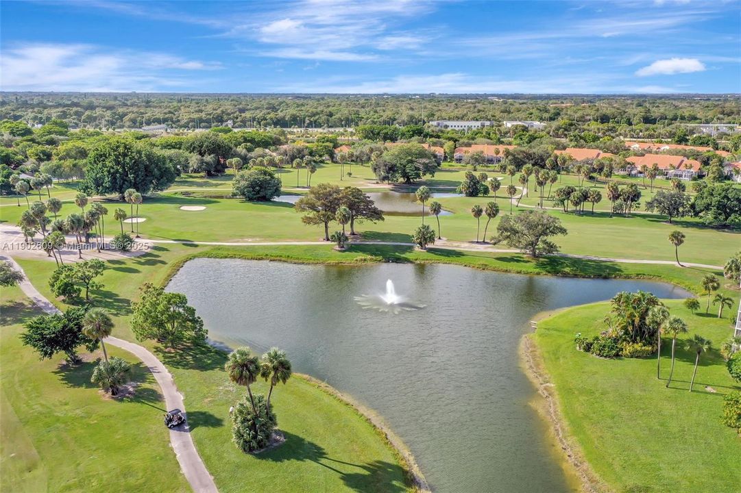 Aerial view of the lush golf course and lake — wide fairways, tranquil water features, and palm-dotted greens wrap the community in resort-style scenery.