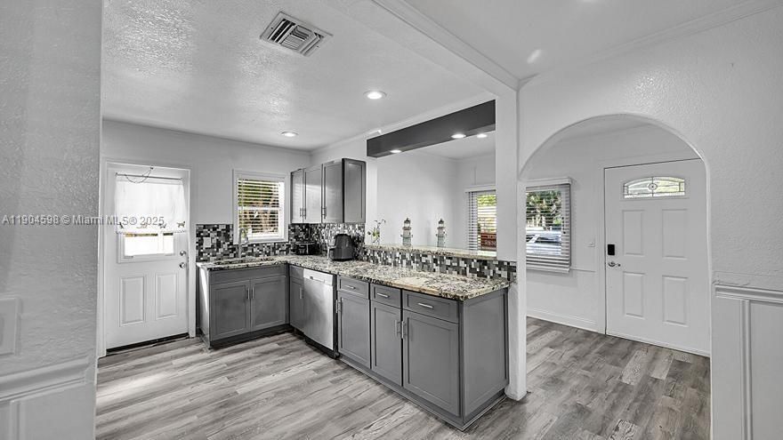 Arched Walkways, Baseboards Wall, Crown Molding, Drywall, Gray Cabinets, Kitchen Peninsula, Natural Light, Opens To Living Area, Pass Through Window, Recessed Lighting, Shaker Cabinets, Stone Countertops, Textured Ceiling, Textured Wall, U Shaped Kitchen, Vent, Wood Finish Floor, Arched Walkways, Drywall, Shaker Cabinets, Textured Ceiling, Vent