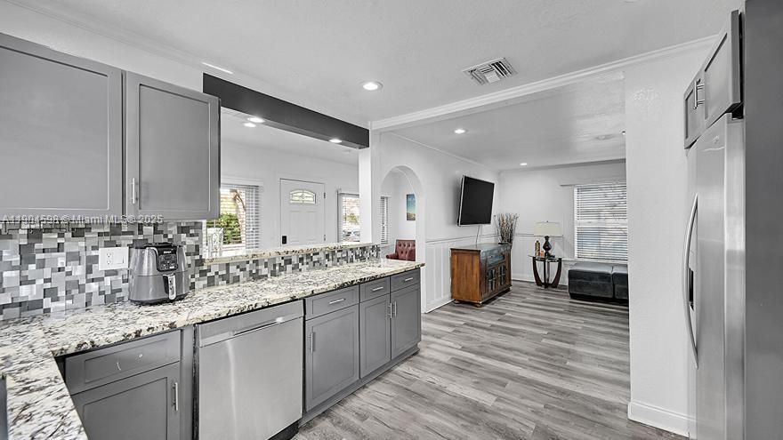 Arched Walkways, Baseboards Wall, Crown Molding, Drywall, Gray Cabinets, Kitchen Peninsula, Natural Light, Opens To Living Area, Pass Through Window, Recessed Lighting, Shaker Cabinets, Stone Countertops, Textured Ceiling, Textured Wall, U Shaped Kitchen, Vent, Wood Finish Floor, Arched Walkways, Drywall, Shaker Cabinets, Textured Ceiling, Vent