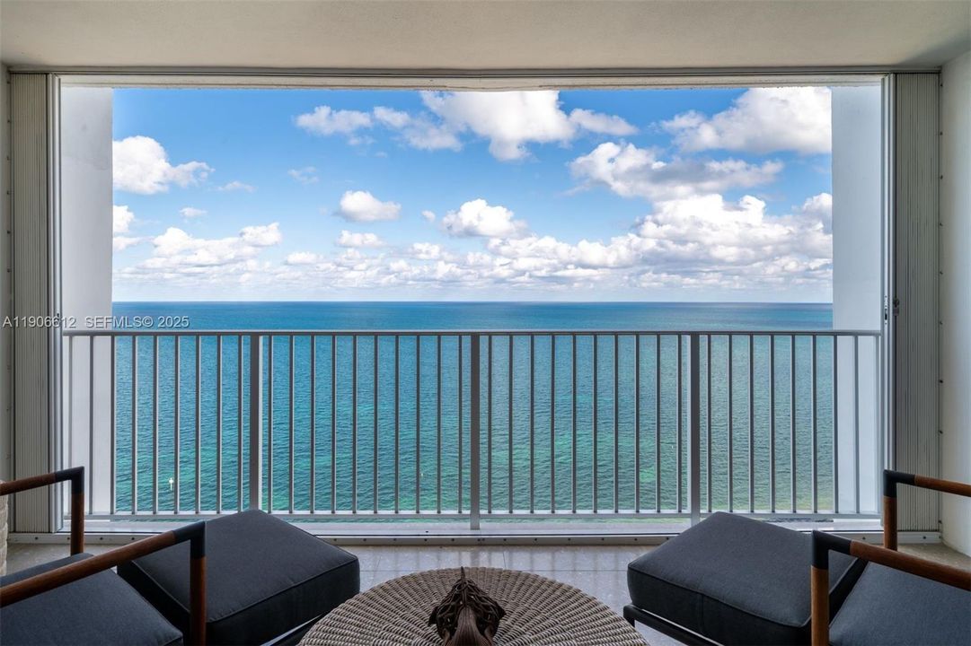 Balcony with high-impact glass doors and seating to enjoy sunrises, ocean breeze, and wave sounds.