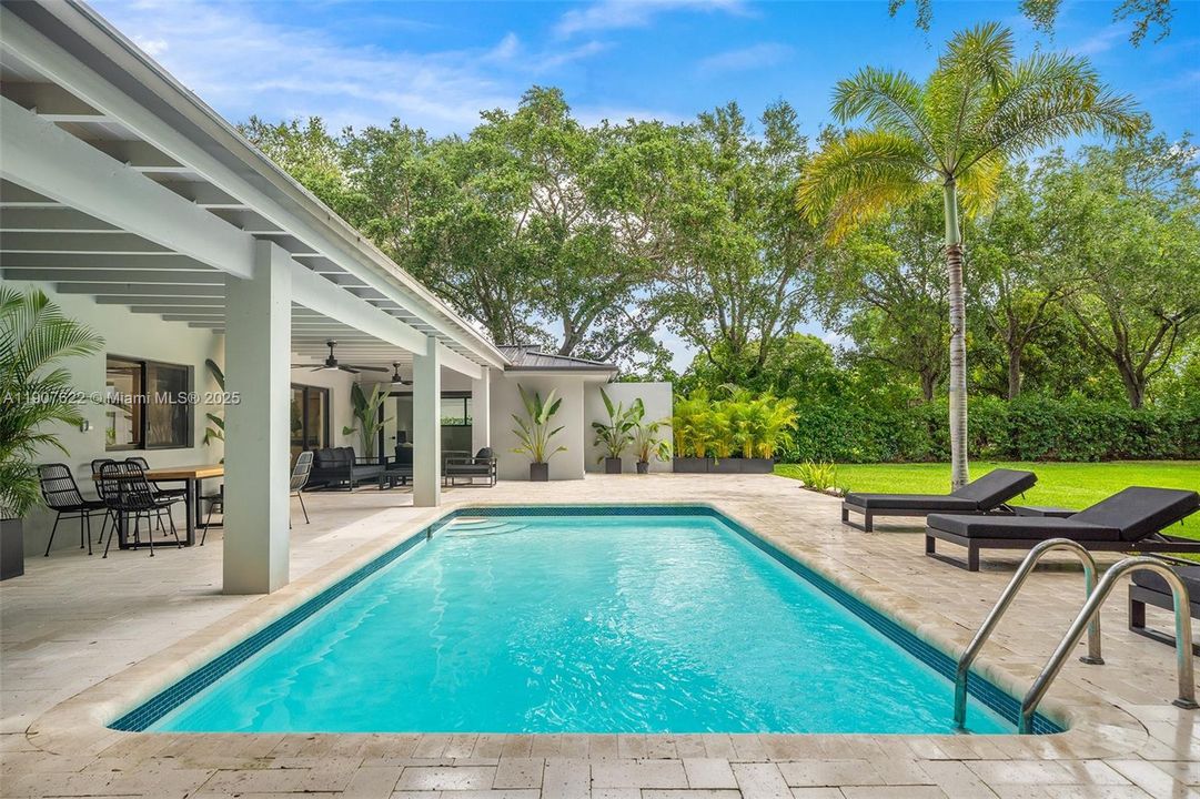The pool steals the spotlight—crystal-clear, oversized, and perfectly framed by lush landscaping and a covered terrace ideal for Miami living.