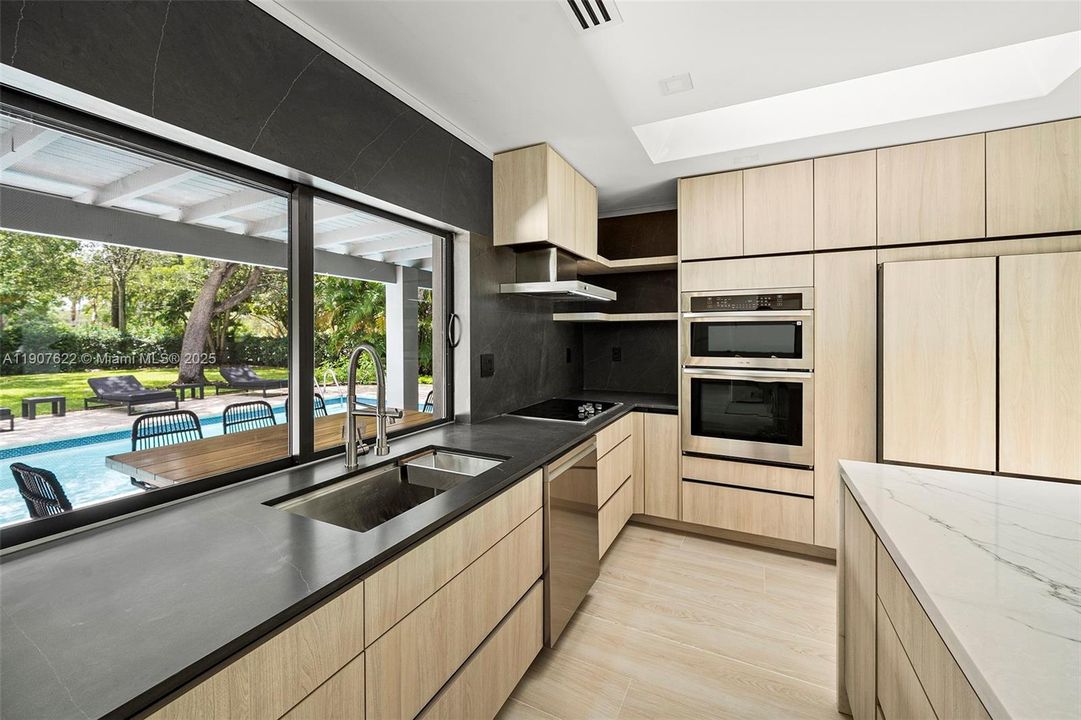 A stunning picture window over the sink frames the garden and pool—bringing in natural light and lush views into the heart of the kitchen.