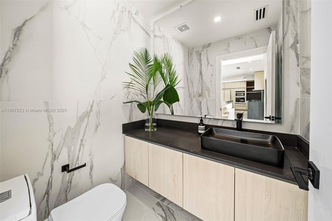 A designer powder room with a rare blend of natural textures—black stone, marble tile, and custom wood cabinetry—designed with bold sophistication.