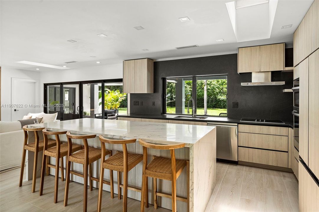 This custom kitchen features exquisite natural quartz countertops, a waterfall island, and sleek wood cabinetry—blending warm textures with bold black stone accents for a refined and contemporary look.
