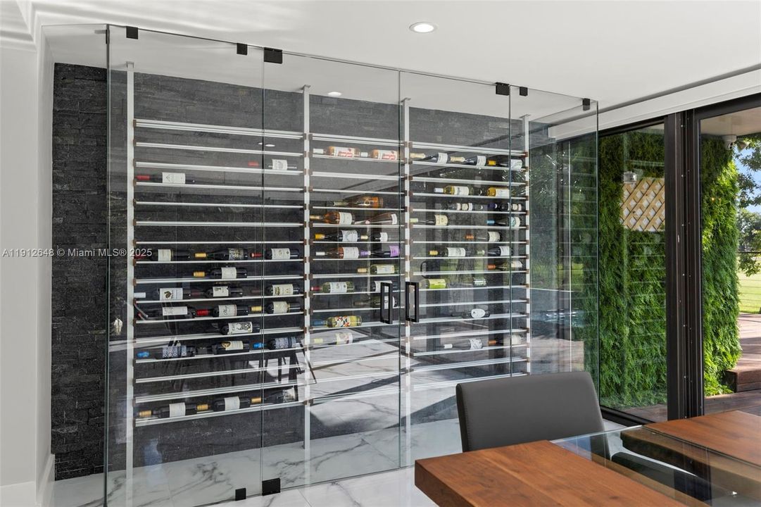 Custom wine display with striking brick-accent wall with built-in wine shelving, enclosed in glass and enhanced with ambient LED lighting.