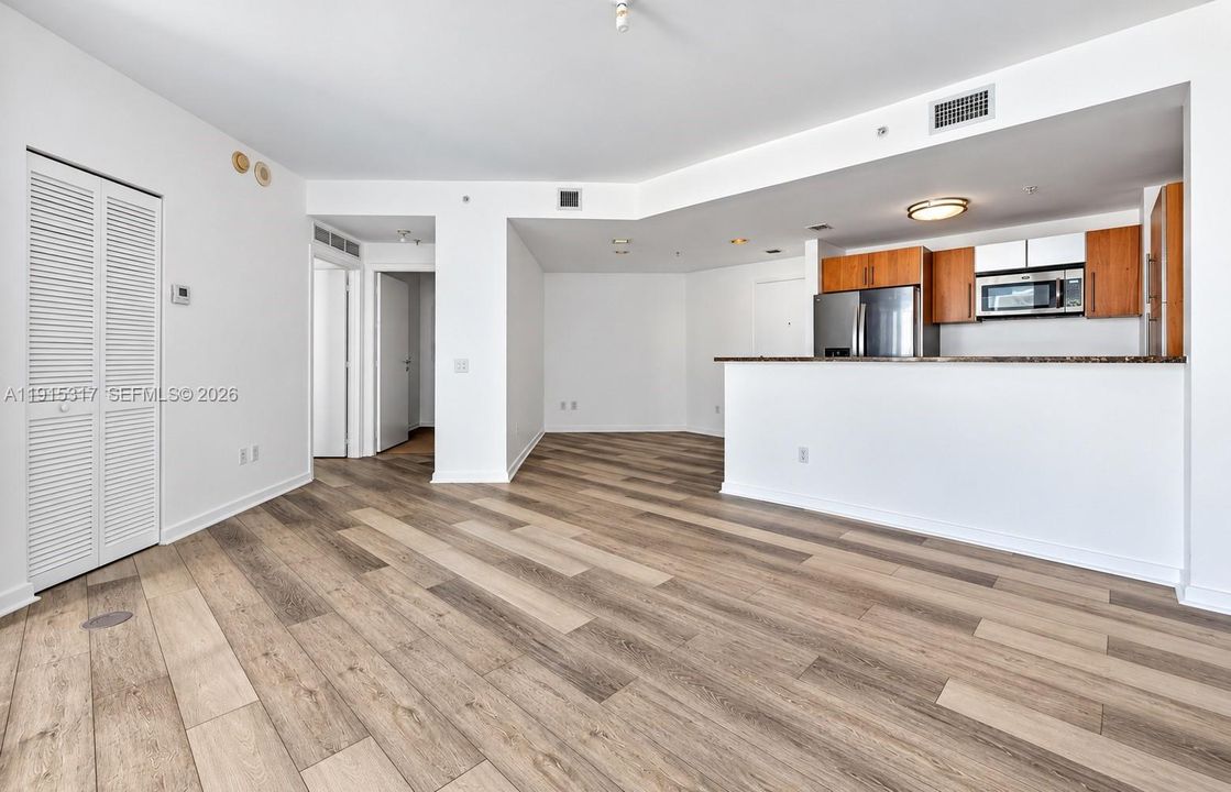 Wood-finish flooring throughout, kitchen with wood cabinetry, stainless steel appliances, and a built-in microwave, white louvered closet doors, and recessed lighting