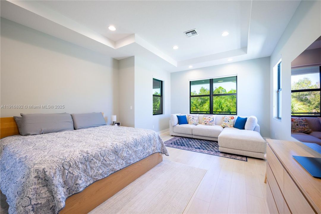 Grand master bedroom with a sitting area and views of nature