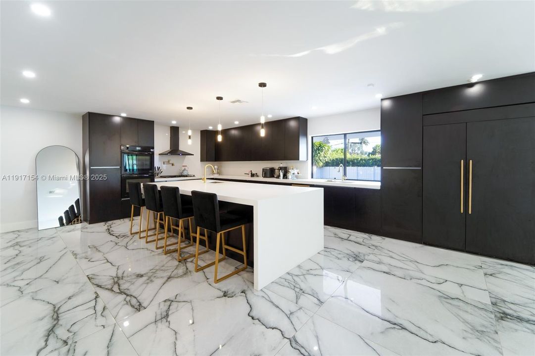 Fully renovated kitchen with black cabinetry, large island, quartz counters, and porcelain floors.