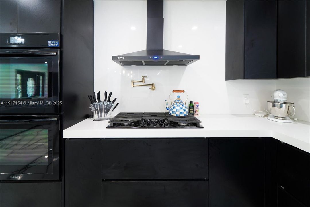 Sleek modern kitchen with gas cooktop, pot filler, custom cabinetry, and quartz counters.