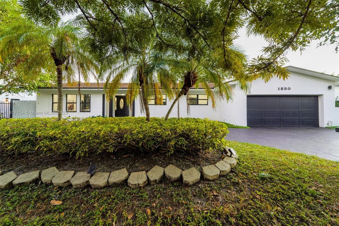 Lush tropical landscaping with mature palms and hedge-lined entry enhancing curb appeal.