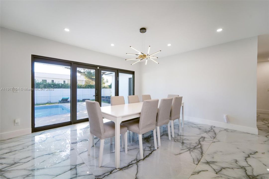 Bright dining area with modern chandelier and pool views through impact sliding doors.