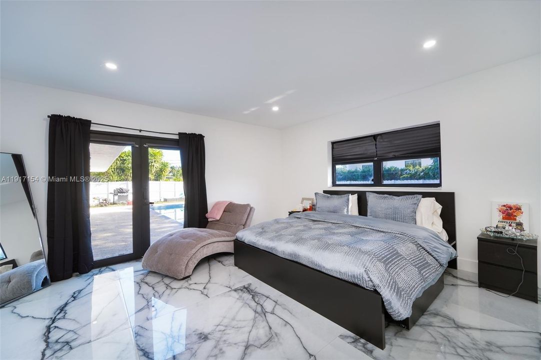 Spacious primary bedroom with pool access, impact doors, and porcelain marble-look flooring.