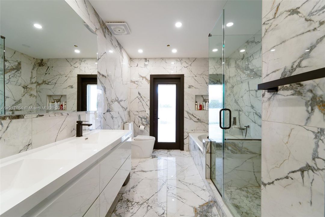 Beautifully renovated full bathroom with marble-look tile, glass shower, soaking tub, and direct pool access.
