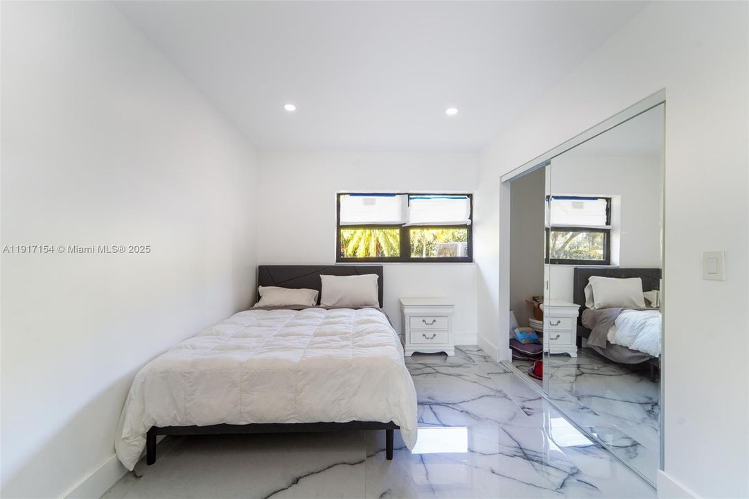 Bright guest bedroom with porcelain flooring, recessed lighting, and mirrored closet doors.