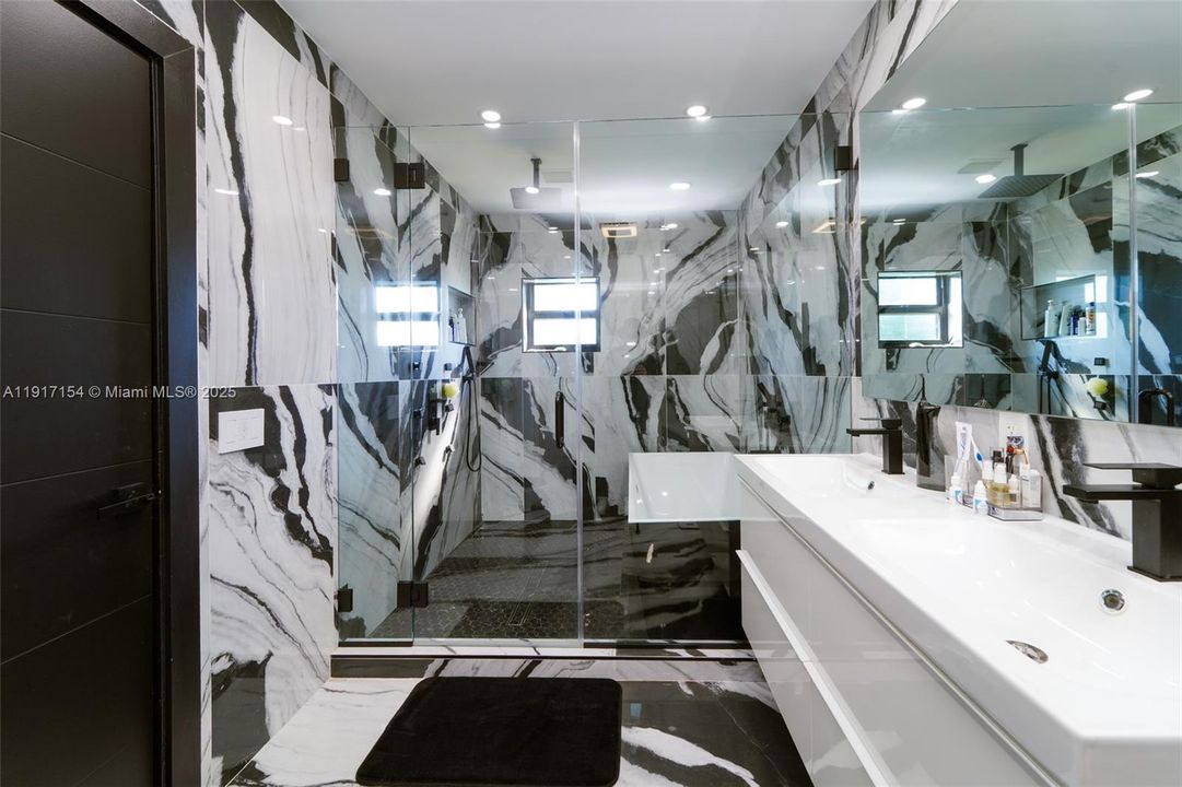 Spa-style bathroom with floor-to-ceiling porcelain tile, glass shower, and modern double vanity.