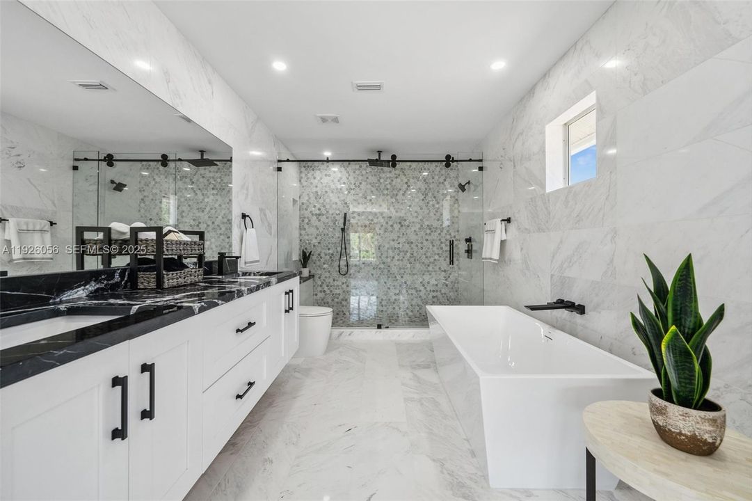 Primary bathroom with dual sinks, tiled walls, glass shower and soaking tub