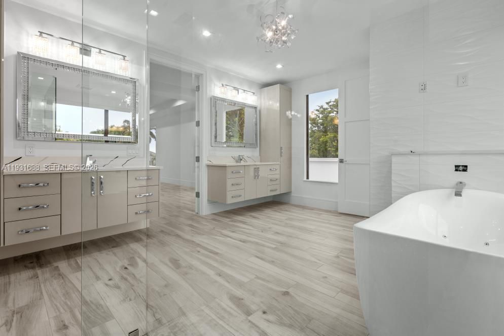 Dual floating vanities with stone-surface countertops, freestanding soaking tub, wood-finish flooring, and recessed lighting